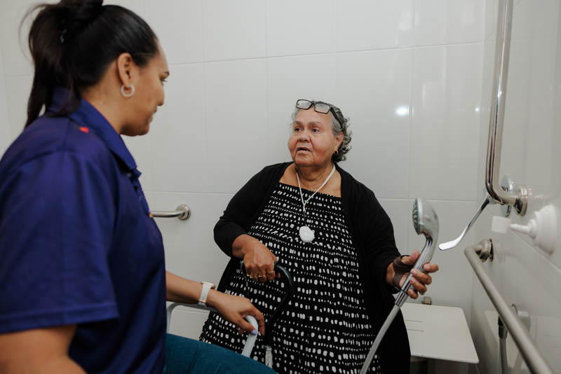 A client with an OT holding a shower head, discussing how they can assist with changes to the house.