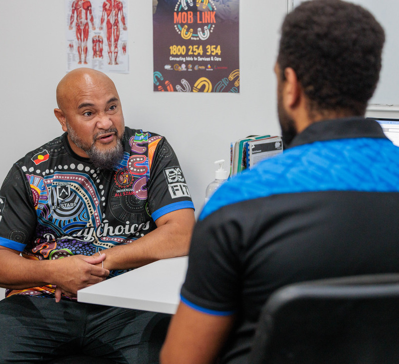 Two men sit across from each other in an office, engaged in a conversation about Bowel Cancer Screening.