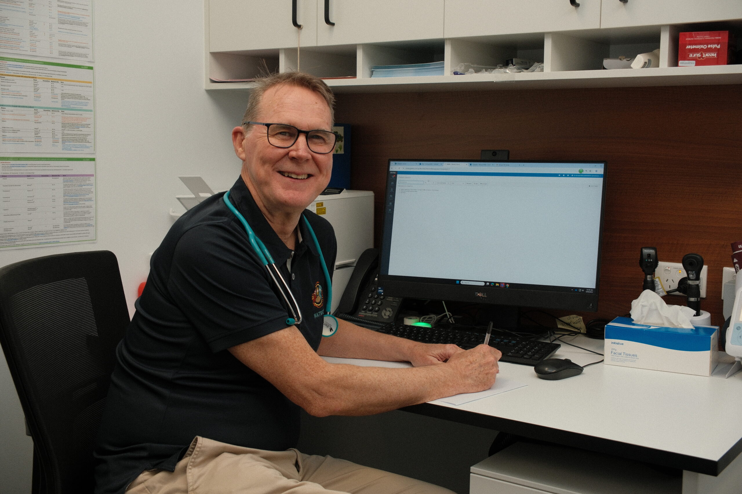 Dr. Richard Mills sits at his desk at Moreton ATSICHS Caboolture, smiling at the camera.