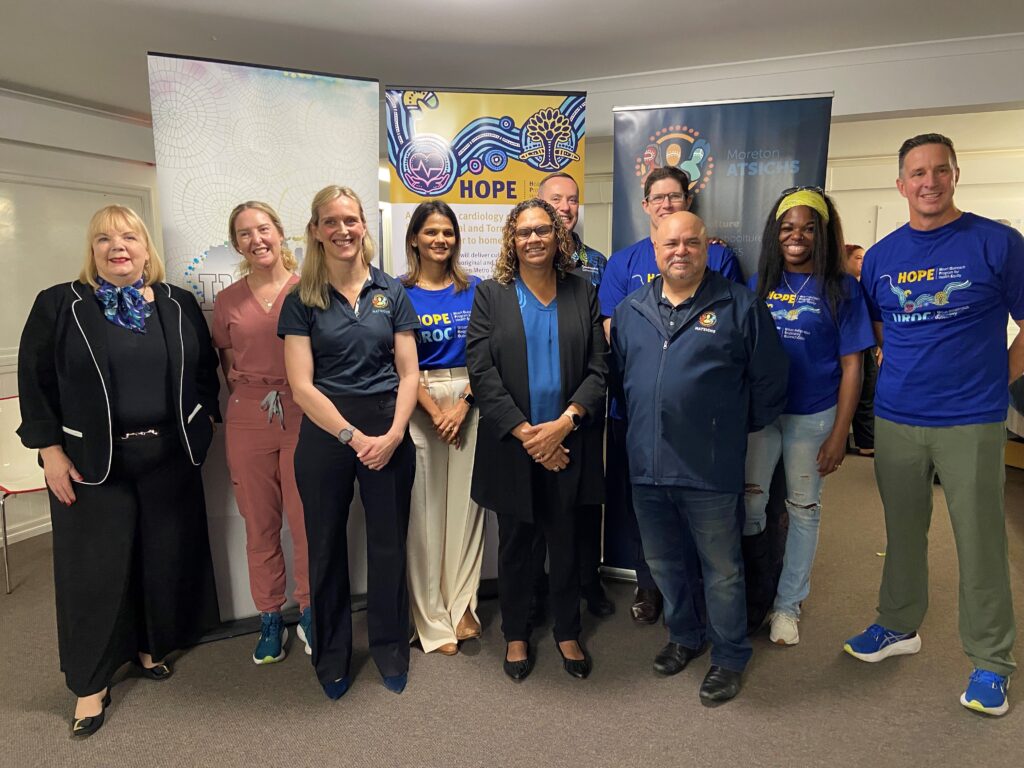 A diverse group of ten people stands and smiles in front of colorful banners at an indoor event, representing HOPE for Mob. Some wear matching blue "HOPE" shirts, while others wear business or casual attire.