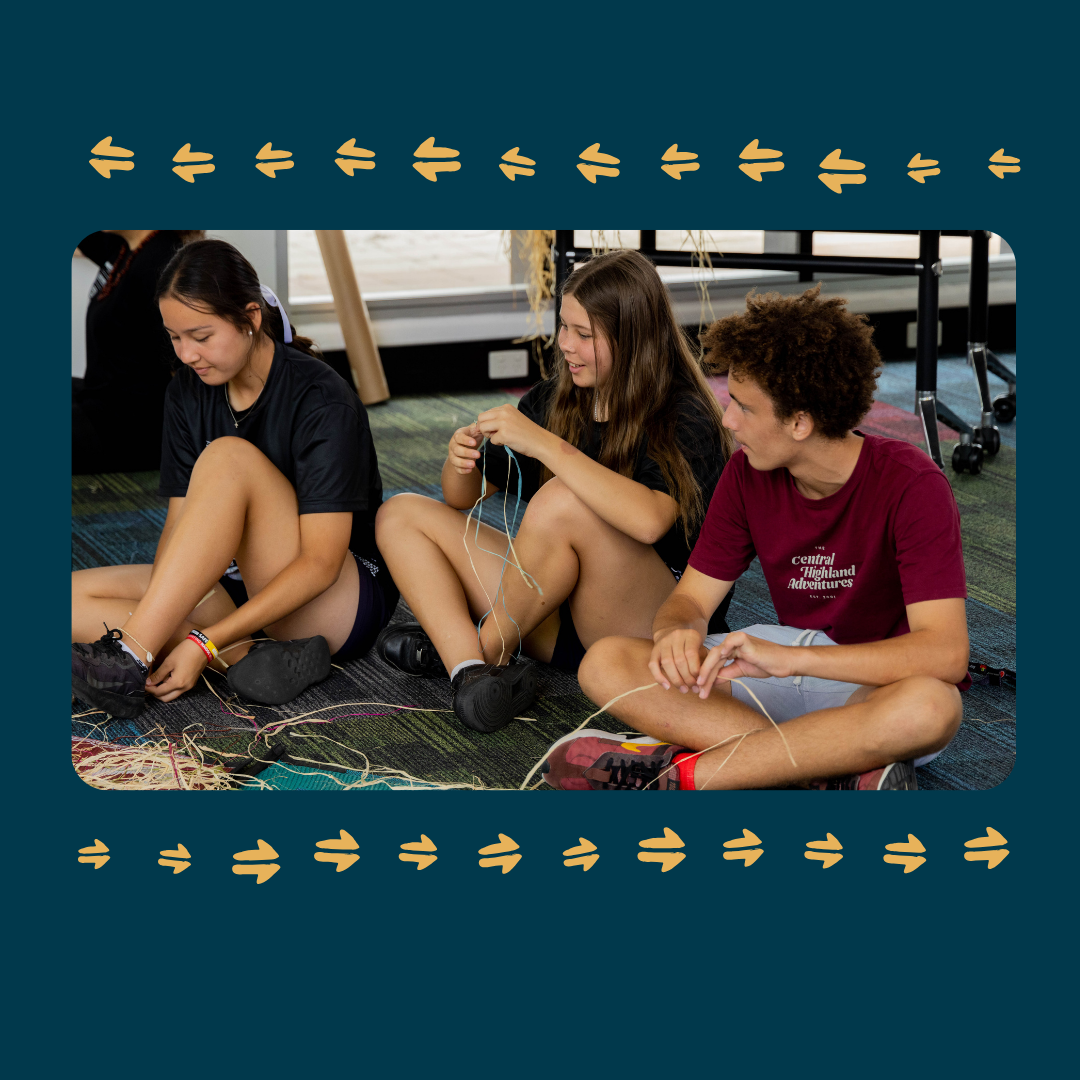 Three young people from the Youth Advisory Group sit on the floor weaving with string, smiling and talking together. The image is framed by a blue border with yellow arrow-like patterns along the top and bottom edges.