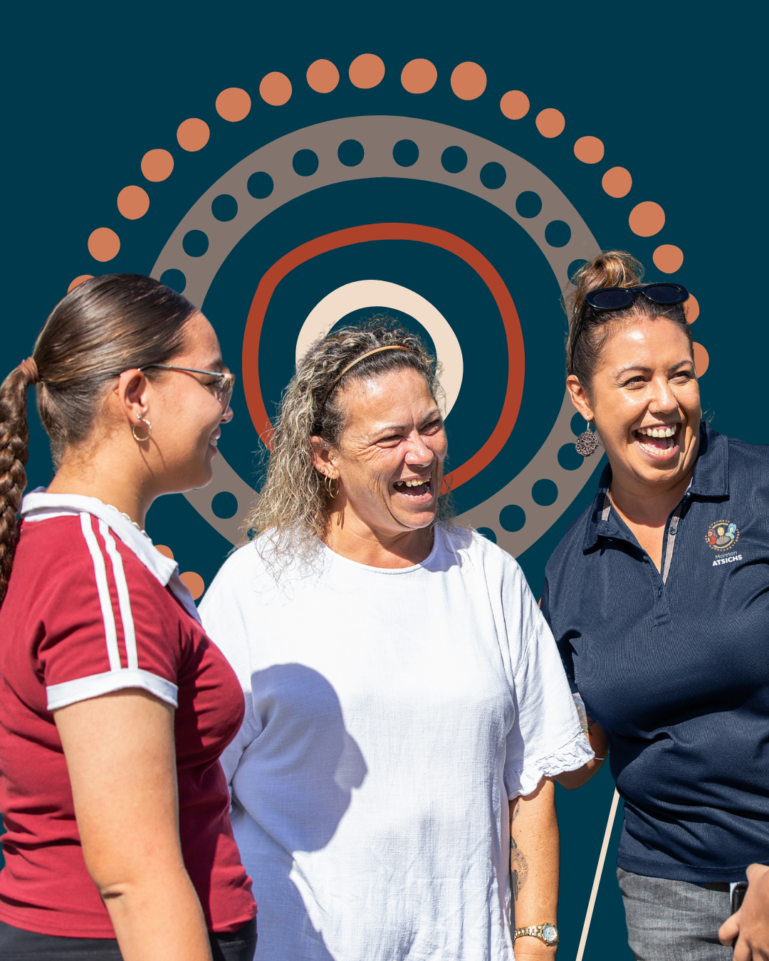 Three women stand together smiling and laughing in front of an Aboriginal-inspired circular dot art design.