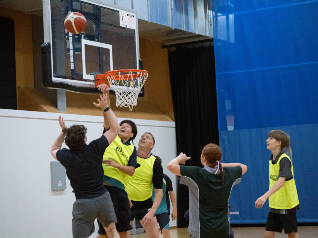 Four players leap near the basketball hoop, while another player watches the shot.